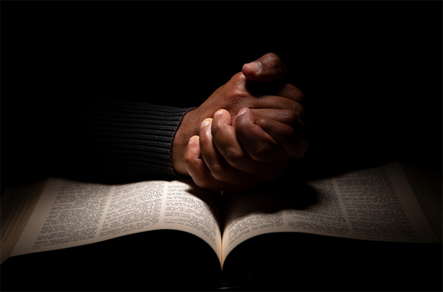 hands in praying position resting on Bible